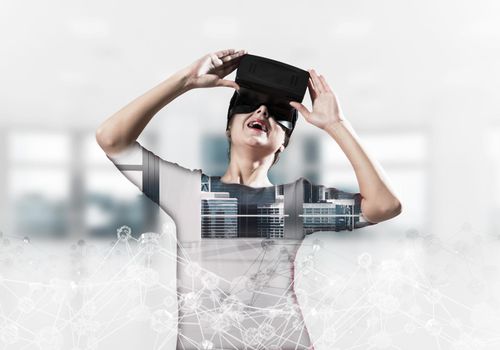 Double exposure of young and beautiful woman in red dress using virtual reality headset while standing indoors of office building with digital network structure.