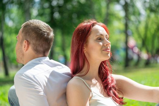 Young couple sits in the park with their backs to each other. Spending time with loved ones