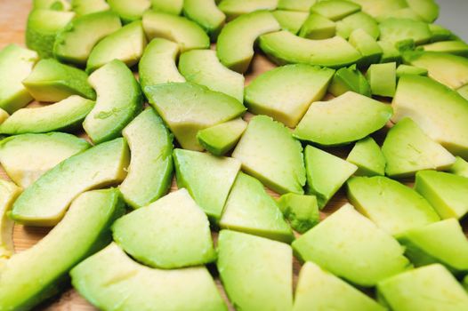 Fresh and tasty avocado cut into pieces laid out on a wooden cutting board. Vegetarian background fresh vegetables.