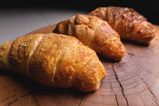 Three French croissants on a wooden cutting board in contrasting light. Fresh treats for breakfast.