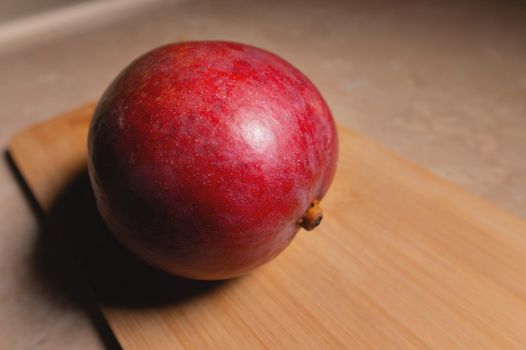 A ripe whole mango fruit lies on a cutting board on a table. Preparing a healthy snack. natural food antioxidants.