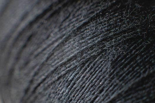 Dark gray spool of thread at extremely high magnification and shallow depth of field. Textile background.