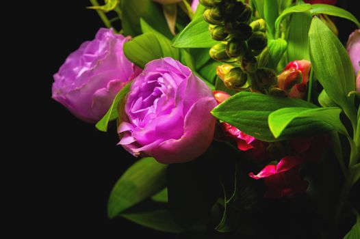 Fresh mixed flower bouquet on black background. Green branches with rich peony roses. Dark floral background.