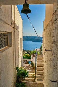 Greek village typical view with whitewashed houses and Aegean sea visible through arch and bell. Plaka town, Milos island, Greece