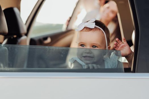 Toddler Caucasian Girl Sitting Inside Car and Waving Hand Imitating Hello Through the Window
