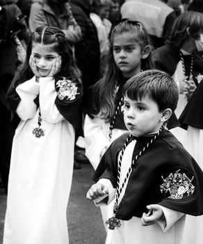 Elche, Spain- April 13, 2022: Children on Easter Parade with bearers and penitents through the streets of Elche city in the Holy Week