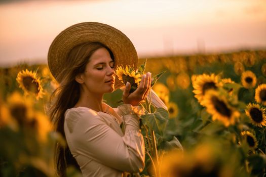 Beautiful middle aged woman looks good in a hat enjoying nature in a field of sunflowers at sunset. Summer. Attractive brunette with long healthy hair