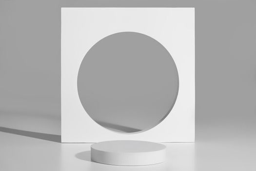 White empty flat cylindrical platform and square element with round opening on gray background. Abstract minimalist podium for product demonstration. Monochrome image