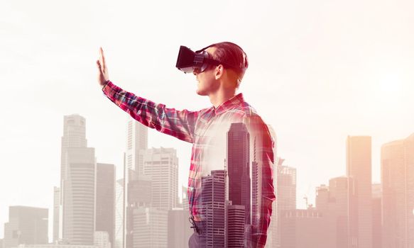 Young man with virtual reality headset or 3d glasses over cityscape background