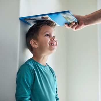 Cropped shot of a little boy getting his height measured against a wall with a book.