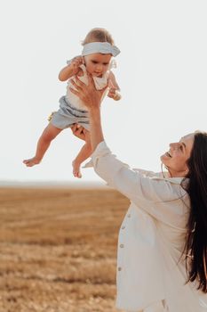 Happy Mother Holding Her Baby in Arms Imitating Flying, Young Mom Playing with Toddler Daughter Outside City at Sunset