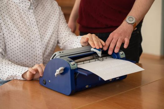 A man teaches a blind woman to type on braille machine