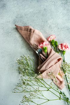 Spring place setting with pink clove flowers on white concrete table