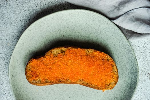 Wholegrain bread toasts with red trout caviar served on stoneware plate