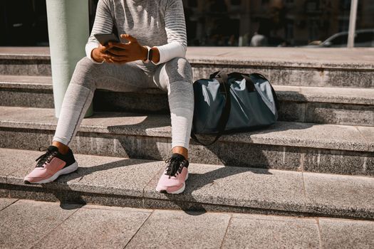 Cropped shot of sporty woman texting using phone while sitting on the stairs after workout