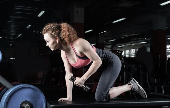 Woman bodybuilder engaged with dumbbells in the gym.