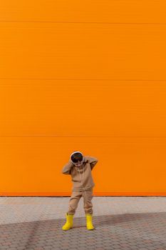 A boy listens to music with headphones on the background of an orange wall . Copy space. Mockup. An article about modern children. An article about modern music. Article about the choice of headphones. Urban lifestyle