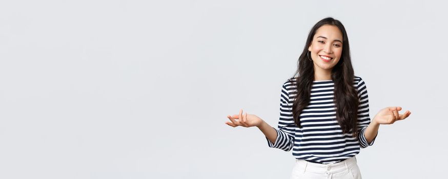 Lifestyle, beauty and fashion, people emotions concept. Smiling cute clueless girl dont have idea, no answer, shrugging with hands spread sideways, standing white background.