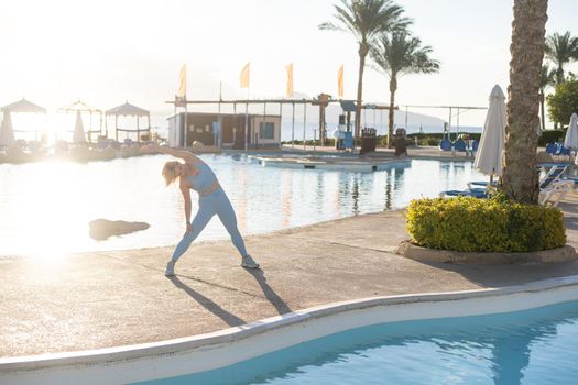 Young woman doing exercise to burn fat, keep fit. Sunset beach, blue sky background. Healthy lifestyle at training camp, outdoor fitness activity, family summer holiday