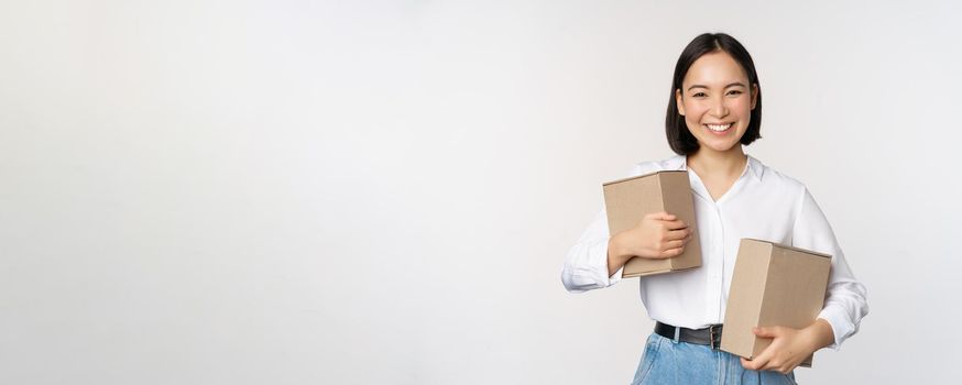 Concept of shopping and delivery. Young happy asian woman posing with boxes and smiling, standing over white background.