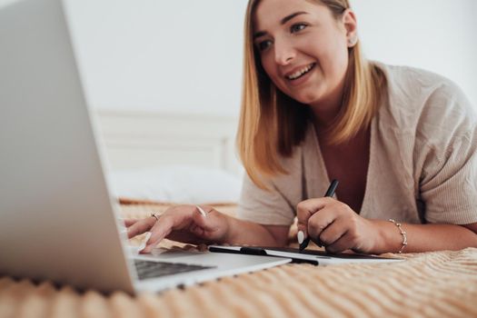 Cheerful Caucasian Woman Laying on Bed in Hotel Room and Working on a Digital Tablet and Laptop, Freelancer at Work, Focus on Pen and Hands