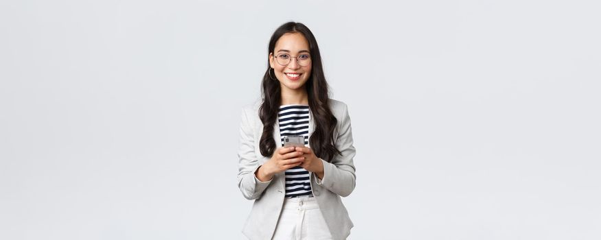 Business, finance and employment, female successful entrepreneurs concept. Smiling pleasant asian businesswoman, real estate broker wear glasses, using mobile phone to contact clients.