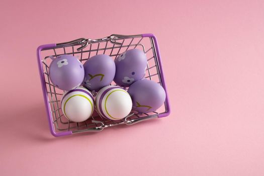 Metal shopping basket with lilac chicken eggs on a pink background. Dietary fresh product. Easter Concept