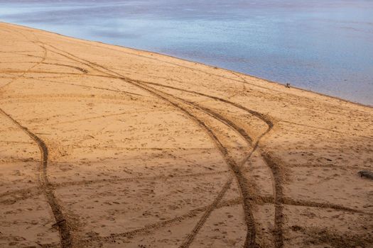 Tire tracks on the sand of an empty beach near the river.