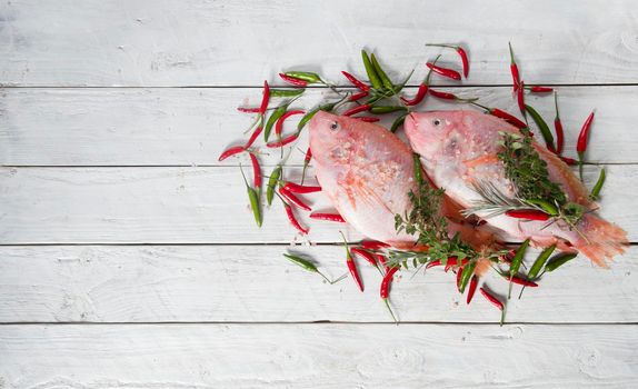 raw fresh pink tilapia fish lies on a board sprinkled with small red and green hot peppers, pink Himalayan salt and garnished with fresh curry sprigs, on white wooden planks. High quality photo