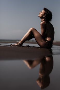 Sexy female body covered with sand. Girl on a beach with sea water reflection.