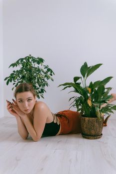 Portrait of young caucasian woman in red cloth laying near flowerpot. Dreamy