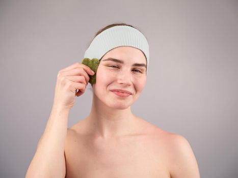 Portrait of a young woman massages her face with a gouache scraper on a white background