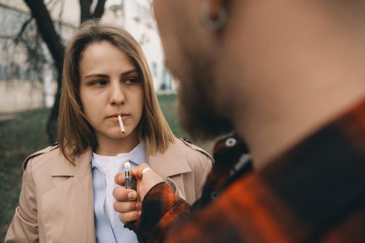 Man lighting womans cigarette at street. hipster