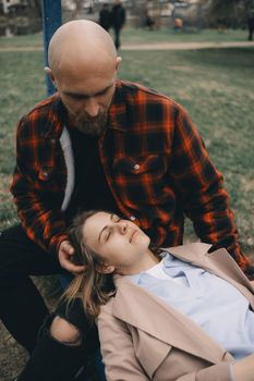 The girl lies on the guy's lap while he strokes her hair. In the park