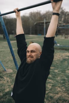 A bald bearded man tries to pull himself up on a horizontal bar in the park