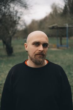 A white man with bald head and beard has a rest in a park, close-up.