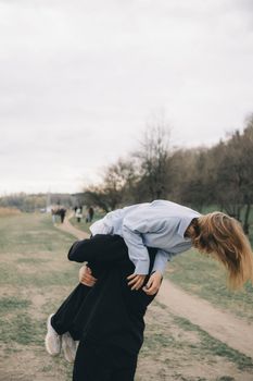 man carries a woman in his arms in the park and they have fun and happy