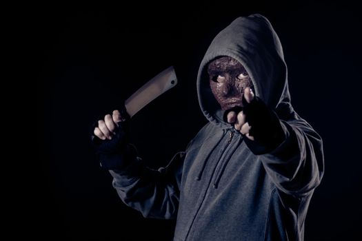 Scary killer in mask and hoodie holding knife and pointing finger