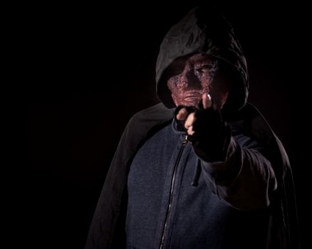Scary killer in mask and hoodie pointing finger