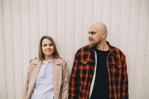 Loving couple stand near wall and look in camera hipster