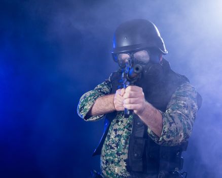 Soldier in army fatigues wearing gas mask holding assault rifle in haze of blue smoke