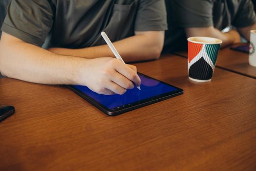 Young creative web designer in casualwear having coffee with cookies and drawing with stylus on tablet while working over new website