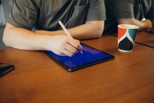 Young creative web designer in casualwear having coffee with cookies and drawing with stylus on tablet while working over new website