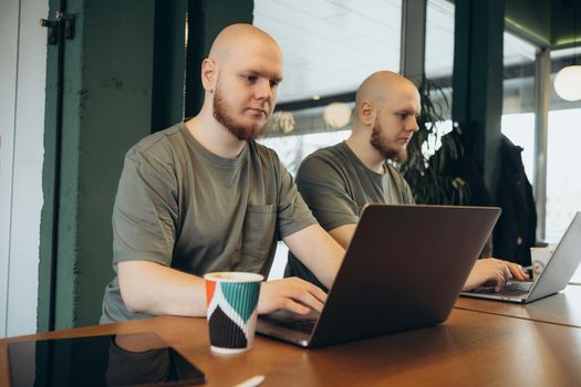 Unshaven happy man smiling and using laptop while sitting in cafe