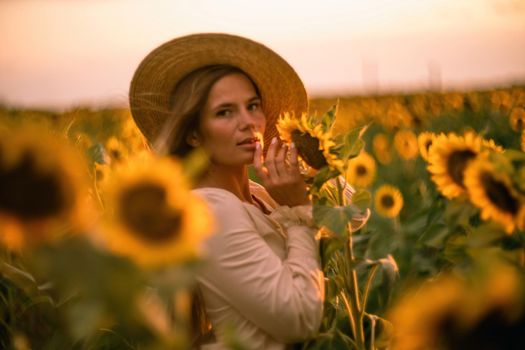 Beautiful middle aged woman looks good in a hat enjoying nature in a field of sunflowers at sunset. Summer. Attractive brunette with long healthy hair