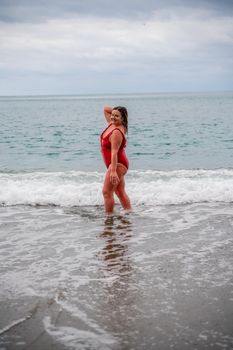 Woman in a bathing suit at the sea. A fat young woman in a red swimsuit enters the water during the surf.