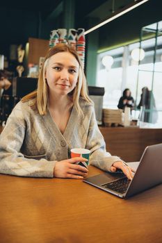 Girl working at her laptop sitting in the cafe happy