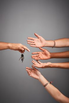 Studio shot of unidentifiable hands reaching for a set of keys against a gray background.