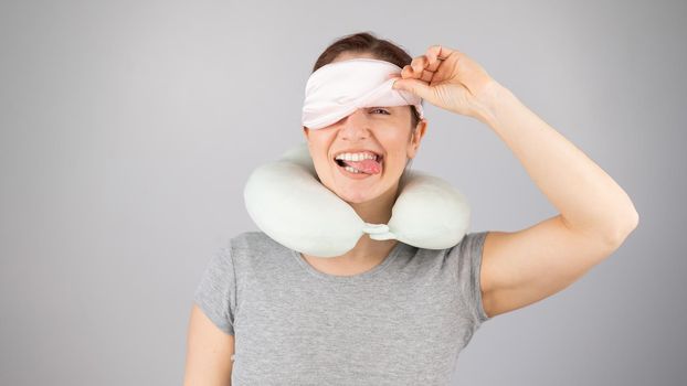 Smiling caucasian woman with a travel pillow takes off her sleep mask on a white background