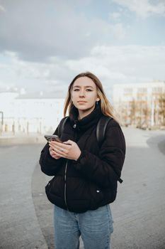 gorgeous beautiful young woman with blonde hair messaging on the smart-phone at the city street background. pretty girl having smart phone conversation in sun flare.